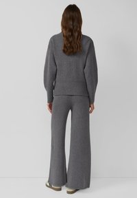 Pull gris en maille avec manches larges et ourlet côtelé, associé à un pantalon gris à jambes larges en texture douce. Chaussures : mocassins beiges avec accents noirs.