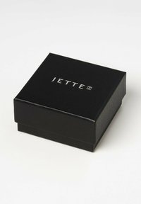Sort rektangulær smykkeboks med en tekstureret overflade, prydet med et sølvfarvet "JETTE" logo på låget. Kompakt og minimalistisk design.