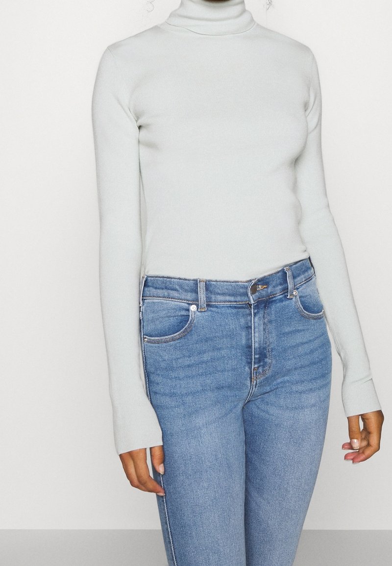 Pull à col roulé bleu clair en tricot côtelé, avec des manches longues et une coupe ajustée, associé à un jean en denim bleu à coupe classique.