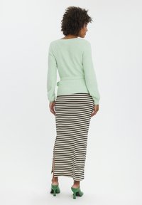 Mintgrøn langærmet sweater med bånd i taljen, parret med en sort og hvid stribet maxi-nederdel med sideslids og grønne højhælede sko.