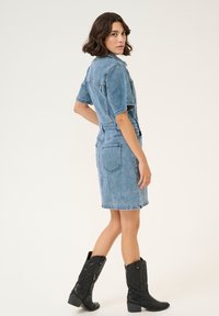 Denimkleit lühikeste varrukatega, helesinine värv, figuuri rõhutav vöökoht ja tagataskud. Kombineeritud mustade cowboy-saabastega, millel on tekstuurilised detailid.