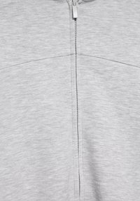 Világosszürke szövet középen függőleges cipzárral és finom vízszintes varrással a felső résznél.