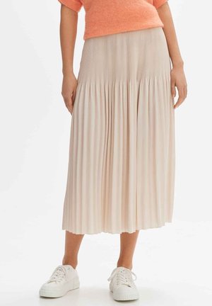 Jupe midi plissée beige avec une large ceinture froncée, associée à des baskets blanches. Texture douce, le tissu léger tombe élégamment.