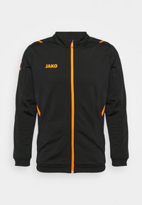 Svart sportjacka med orange detaljer, hel dragkedja, hög krage och sidfickor. Har logotyp på bröstet och kontrasterande axelränder.