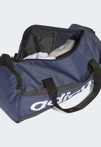 Borsa duffel blu navy realizzata in tessuto resistente, con manici neri e logo bianco. L'apertura con zip rivela abbigliamento riposto.