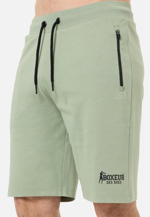 Jasnozielone szorty z czarnymi sznurkami, kieszenią na suwak po boku oraz logo „Boxeur des Rues” w pobliżu dolnej krawędzi, noszone przez męskiego modela.