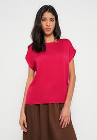 Růžová halenka s krátkými rukávy a kulatým výstřihem z lesklé saténové látky. Hladká textura, volný střih s vrstveným lemem. Kombinováno s hnědou texturovanou sukní.