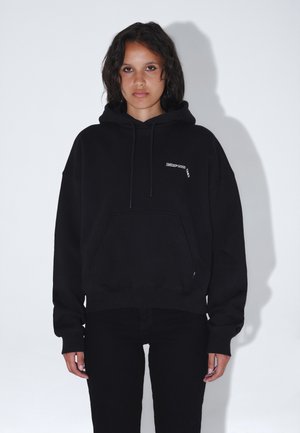 Sort hættetrøje med en frontlomme, prydet med et lille hvidt logo på brystet. Ribstrikkede manchetter og kant. Stoffet ser blødt og hyggeligt ud.