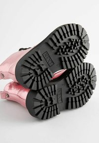 Bottines métalliques roses avec semelles en caoutchouc noir présentant un motif de semelle texturé. Design à lacets avec œillets renforcés.