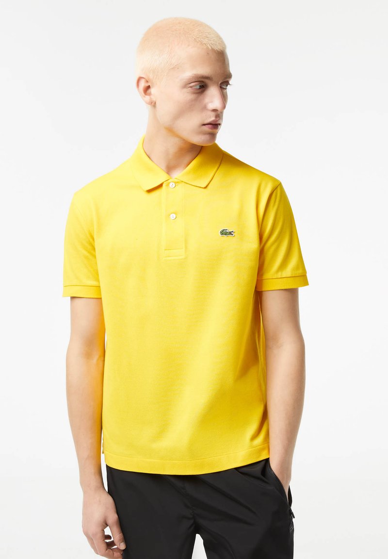 Polo shirt in cotone giallo con colletto classico, pattina con tre bottoni e logo ricamato verde sul lato sinistro del petto. Maniche corte.