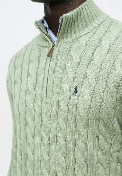 Ανοιχτό πράσινο πουλόβερ με πλέξιμο, ψηλό γιακά και φερμουάρ, με μικρή απεικόνιση λογότυπου. Υφή, μαλακό ύφασμα.
