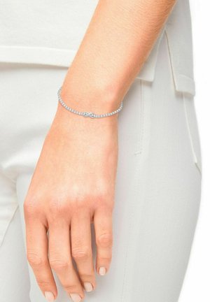 Silbernes Armband, verziert mit kleinen klaren Kristallen, mit einem Infinity-Symbol-Design in der Mitte, getragen an einem hellhäutigen Handgelenk.