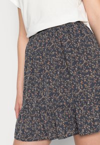 Saia com estampa floral featuring um fundo azul escuro, com uma bainha franzida, cintura elástica e pequenos padrões de flores laranja e bege.