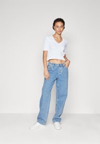 T-shirt blanche à col en V cropped, associée à un jean en denim bleu clair à coupe ample et des baskets blanches. Texture lisse avec un design décontracté.