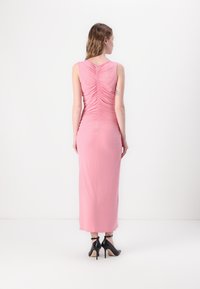 Pink sleeveless dress with gathered detailing at the back, reaching mid-calf length. Worn with black ankle-strap high heels.