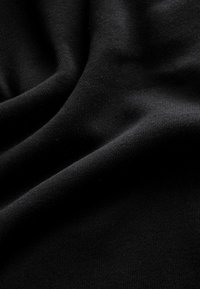 La tela de punto negra presenta una textura suave con costuras finas y uniformes, mostrando un caído suave y un ligero brillo a la luz natural.
