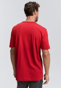 Rotes Baumwoll-T-Shirt mit kurzen Ärmeln und rundem Halsausschnitt. Die Rückansicht zeigt eine glatte Textur ohne sichtbare Muster oder Akzente.