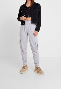 Czarna dżinsowa kurtka, skrócona długość, srebrne guziki; szare spodnie dresowe z elastyczną talią i bocznymi kieszeniami; beżowe sneakersy z grubą podeszwą.