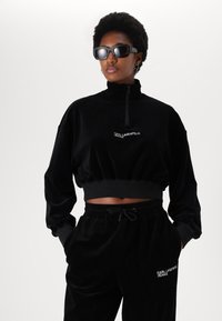 Black corduroy zip-up cropped sweatshirt with long sleeves and logo, paired with matching relaxed-fit pants featuring an elastic waistband.
