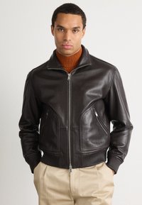 Giacca bomber in pelle marrone con chiusura a zip, polsini a costine e tasche laterali. Presenta un colletto classico e una texture liscia.