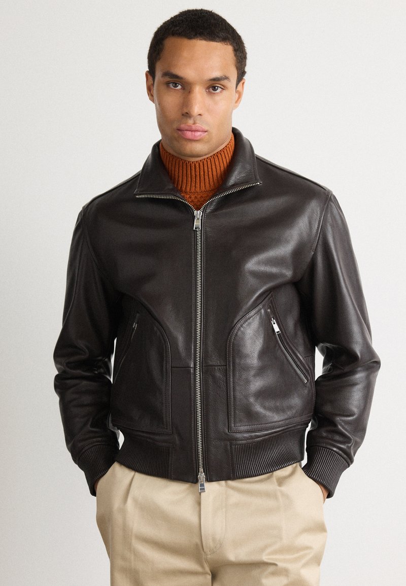 Giacca bomber in pelle marrone con chiusura a zip, polsini a costine e tasche laterali. Presenta un colletto classico e una texture liscia.