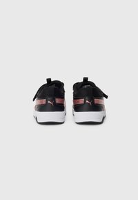 Une paire de baskets noires et rose doré de Puma vue de l'arrière avec des semelles blanches, affichée sur un fond clair uni.