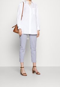 Vit långärmad skjorta med en enkel ficka, kombinerad med blå och vita randiga, tapered byxor. Bruna klacksandaler och en brun handväska.