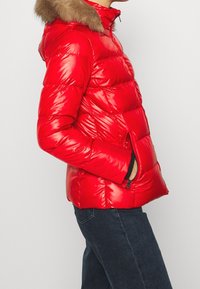 Rød pufferjakke med en skinnende, quiltet tekstur, der har en faux fur hætte og lynlåslommer. Designet til varme og komfort.