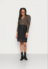Blusa de padrão floral com ombros almofadados, combinada com uma saia plissada preta e botas pretas até ao tornozelo. Óculos de sol redondos incluídos.