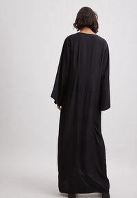 Černé šaty s dlouhými rukávy a splývavým siluetou, vyrobené z jemného materiálu. Mají kulatý výstřih a široké rukávy, které sahají do poloviny lýtek.
