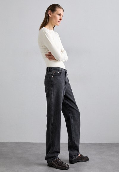 Black denim jeans with a relaxed fit, featuring a high waist, side pockets, and subtle stitching details. Paired with a light long-sleeve top.