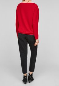 Red textured knitted top with a wide neckline, paired with black slim jeans and black ankle boots with a pointed toe and curved accents.