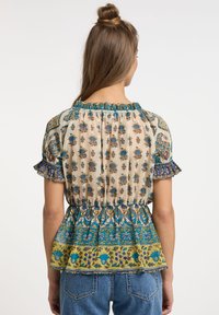 Top peplum floreale in beige chiaro con motivi blu e verdi, maniche arricciate e vita elasticizzata. Tessuto morbido e leggero.