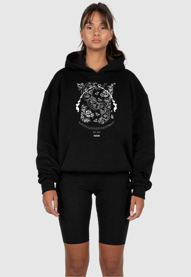 Svart hettegenser med blomsterdesign i hvitt, med kengurulomme, kombinert med svarte biker-shorts for et monokromatisk utseende.