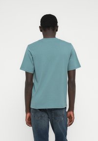 Τιρκουάζ βαμβακερό t-shirt με κοντά μανίκια και στρογγυλή λαιμόκοψη, σε φωτογραφία από πίσω, συνδυασμένο με μπλε τζιν παντελόνι. Λείο ύφασμα, απλός σχεδιασμός.