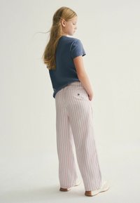 Růžové a bílé pruhované široké kalhoty s volným střihem, v kombinaci s námořnickým tričkem. Kalhoty mají boční kapsy a malý detail loga.