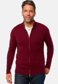 Burgunderfarbener Reißverschluss-Pullover mit gerippten Bündchen und Saum, aus einem weichen Material. Verfügt über einen hohen Kragen und eine lässige Passform, über einem weißen Hemd getragen.