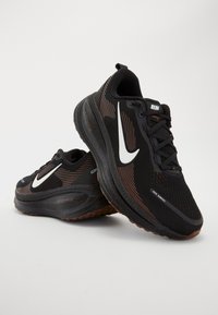 Paire de chaussures de course Nike noires avec logos swoosh blancs, semelles texturées et tissu en mesh, positionnées sur un fond clair uni.