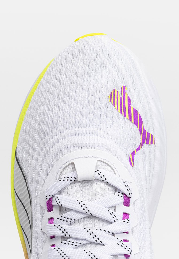 Baskets blanches de sport avec une tige en maille texturée, des accents violets et jaunes, et un logo rayé. Les lacets sont blancs avec des touches de violet.