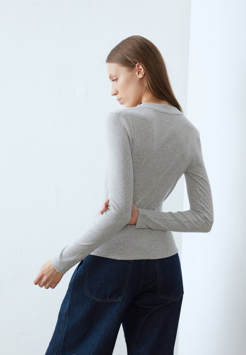 Top grigio a maniche lunghe con design aderente, texture a coste e scollatura rotonda, abbinato a pantaloni a gamba larga in denim scuro.