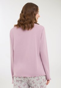 Maglietta lilla a maniche lunghe con orlo arrotondato e bordi sfilacciati, abbinata a pantaloni grigi con un motivo a farfalla nei toni del rosa.
