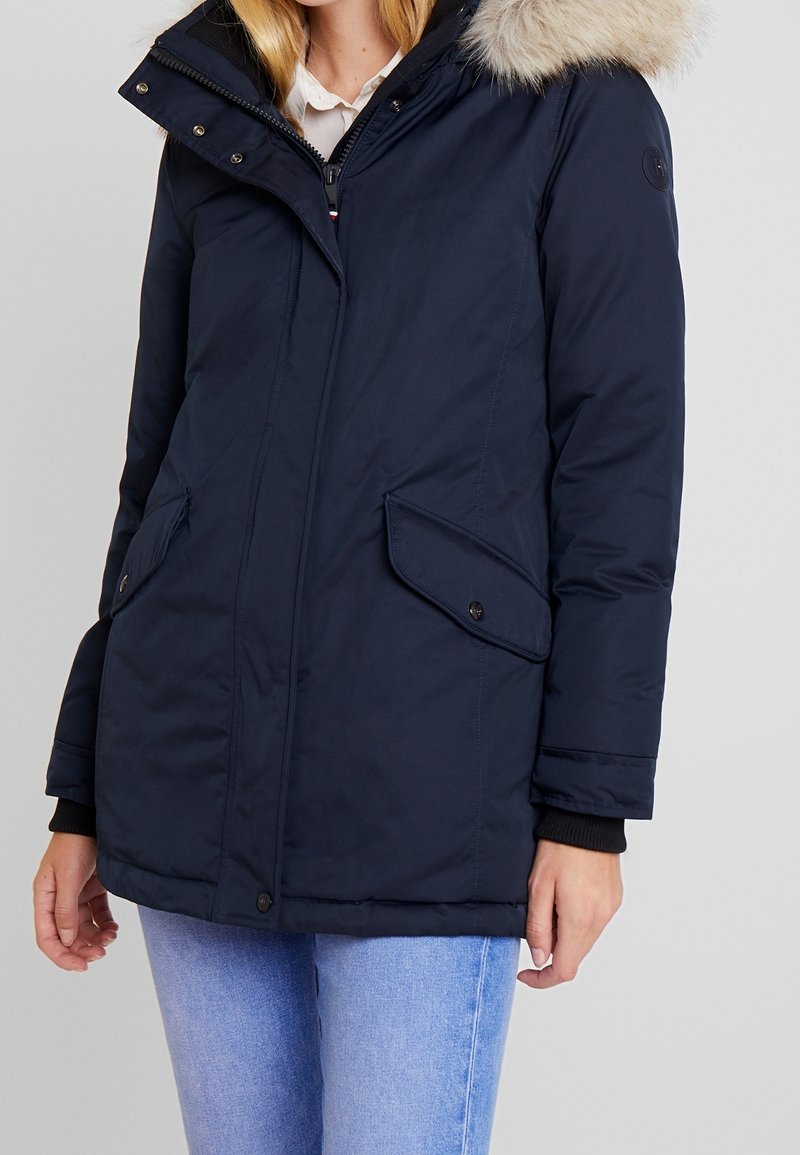 Mörkblå vadderad parka jacka med en huva klädd med konstpäls, framfickor, dragkedjestängning och ribbad manschett. Slät yta.