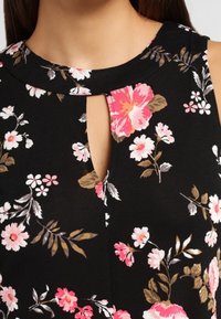 Schwarzes ärmelloses Oberteil mit floralen Motiven in Pink und Weiß, runder Ausschnitt und einem Schlüssellochausschnitt auf der Vorderseite.