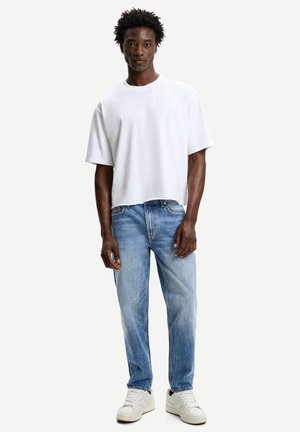 White, oversized cotton t-shirt with short sleeves, paired with light blue, straight-leg denim jeans. Footwear features white sneakers.