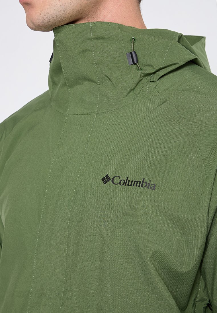 Groene buitenjack met een hoge kraag, gemaakt van textuurstof. Heeft verstelbare hardware en een zwart Columbia-logo op de borst.
