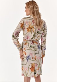 Šaty z ľanovej tkaniny s kvetinovým vzorom, ktoré majú multicolor kvety na smotanovom pozadí, dlhé rukávy a priliehavý strih s detailom na gombíky.