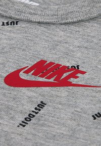 Siva majica s kapuljačom s crvenim Nike logotipom. Crni tekst "just do it" ispisan je više puta oko logotipa. Mekana tekstura, okrugli izrez na vratu.