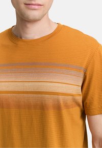 Kortærmet orange skjorte i struktureret stof med horisontale striber i beige og brun henover brystet. Rund halsudskæring.