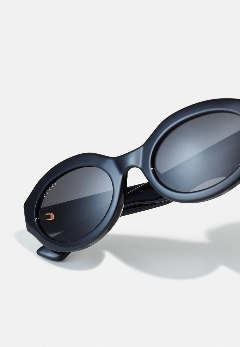 Black oversized sunglasses with round lenses, a matte finish, and geometric edges. Features gold accents on the inner side.