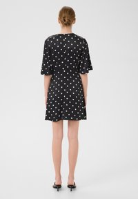 Rochie neagră cu buline albe, mâneci scurte și evazate, cu o siluetă fluidă. Material neted, cu o croială casual, relaxată.